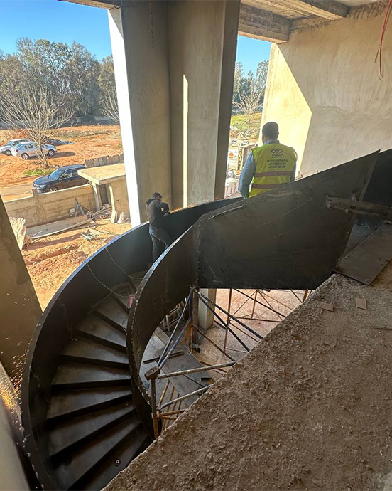 Installation sur chantier d’un grand escalier métallique courbe dans un bâtiment en construction